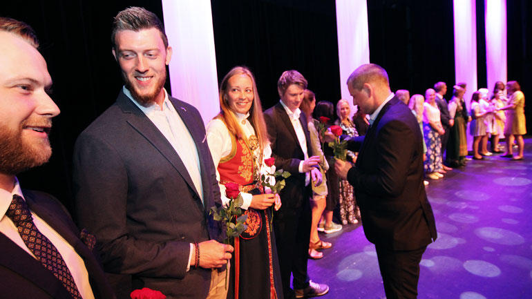Pyntede bacehlorstudenter på idrettsdag får utdelt roser på scenen i Bakkenteigensalen. 