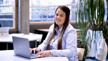 Kvinnelig student sitter smilende foran en laptop. 
