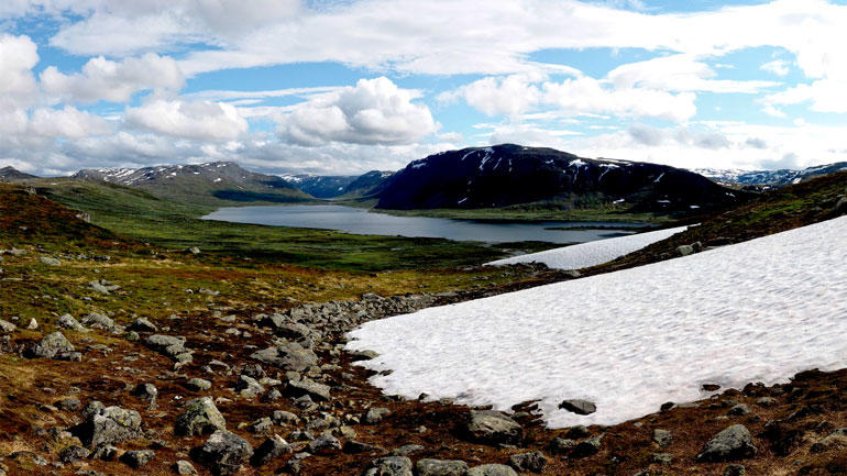 Landskapsbilde av fjell med snø og innsjø i bakgrunnen