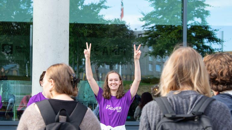 fadder løfter hendene i været og viser seierstegnet foran nye studenter ifm studiestarten 2021 på campus Vestfold