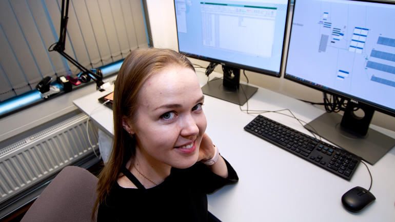 Mariia foran PC-skjermen med hennes digitale simuleringsmodell, snur seg mot kamera fra kontorstolen og smiler. 