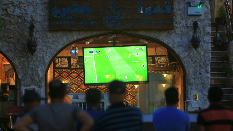 Menn ser på fotball på en storskjerm utendørs i Doha i Quatar. Foto