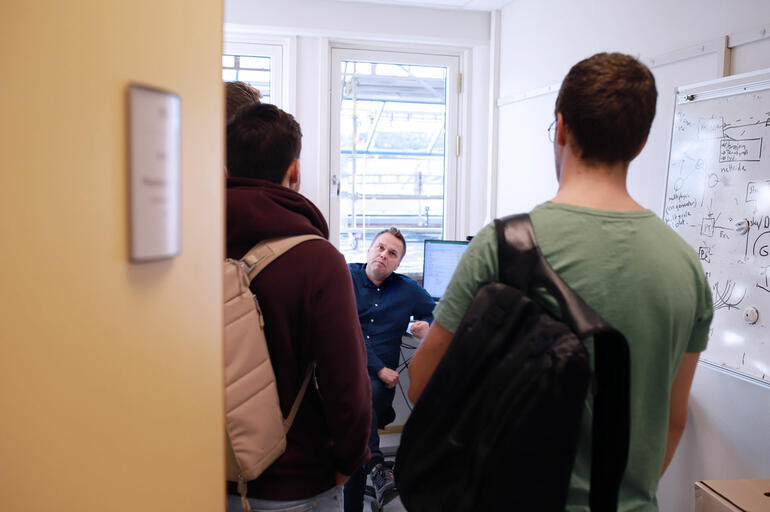 Thomas Øyvang sittende på kontoret og prater med to studenter som står i døra 