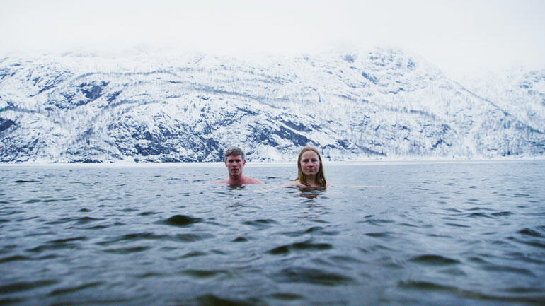 ein mann og ei kvinne badar vinterstid med høge fjell i bakgrunnen. Foto