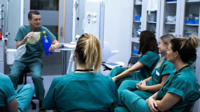 Masterstudenter ikledd grønne operasjonsklær på læring i praksis i sykehussimulator på campus