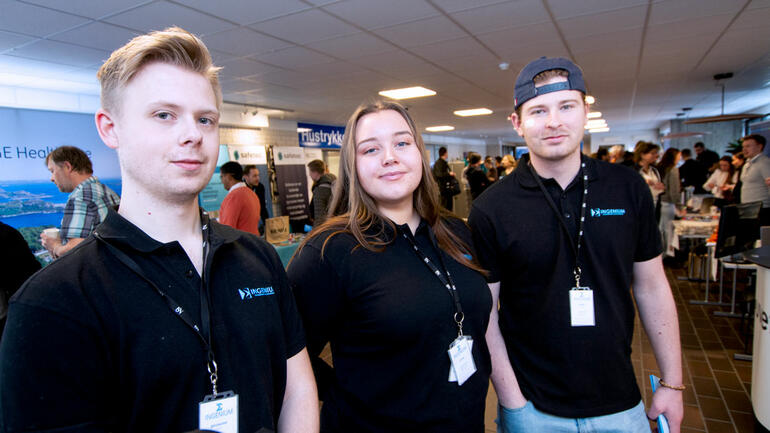 Portrett av ingeniørstudentene Mathias, Kristine og Espen på en rekke med Like t-skjorter med logo til linjeforeningen Sum Ingenium. 
