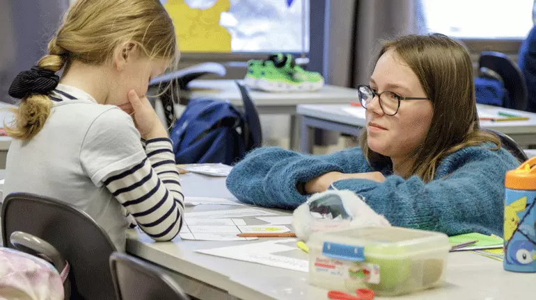 ung lærer i dialog med barneskoleelev i et klasserom