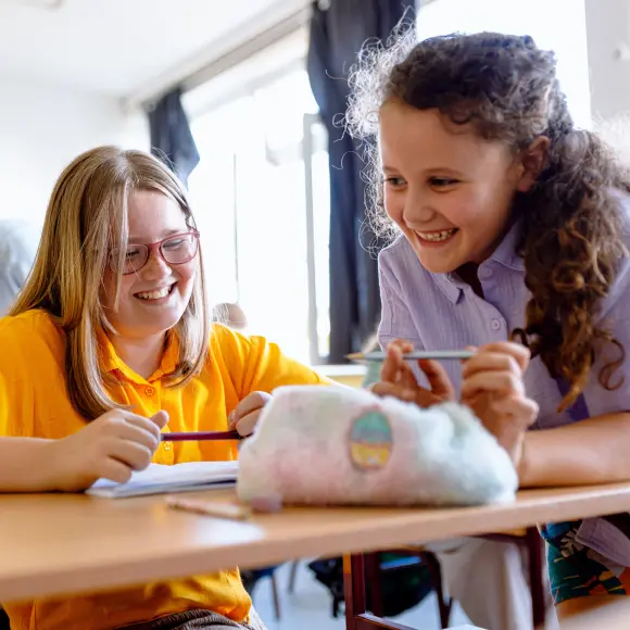 To elever smiler og ler i klasserom mens de jobber med skoleoppgave