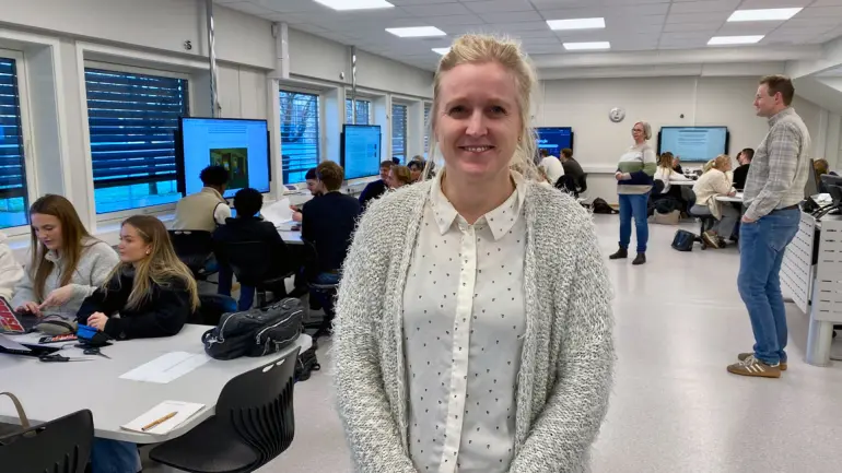 smilende dame foran datarom med ungdommer i gruppearbeid