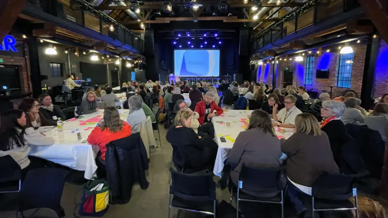 stort konferanserom med mange folk samlet rundt gruppebord.