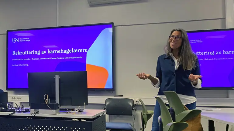 dame gestikulerer foran skjerm der det står "rekruttering av barnehagelærere"