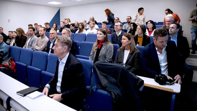 Terje Aasland sittende i auditoriet med mange studenter og ansatte