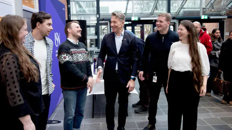 Your Extreme-studentene står på rekke og ser, snakker og smiler med energiministeren i midten.