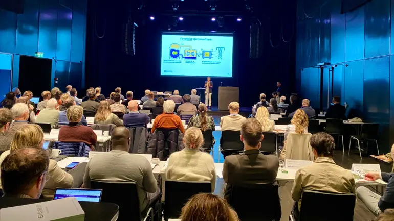 konferansesal sett fra bakerste rad. mange rader med folk sitter og ser på presentasjon om kjernekraft