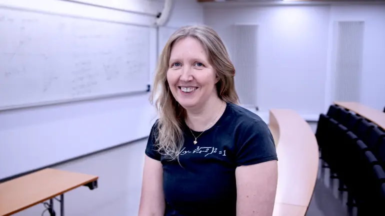 Portrett av Karina sittende i auditorium der hun underviser og med tavla i bakgrunnen 