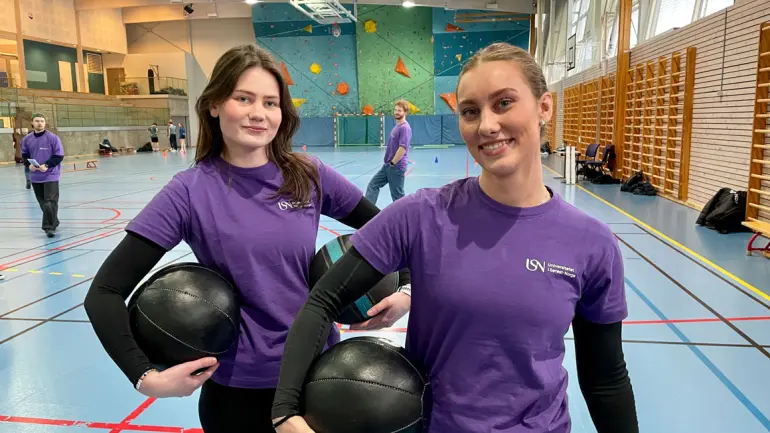 to unge damer holder medisinball under armene og smiler i kamera