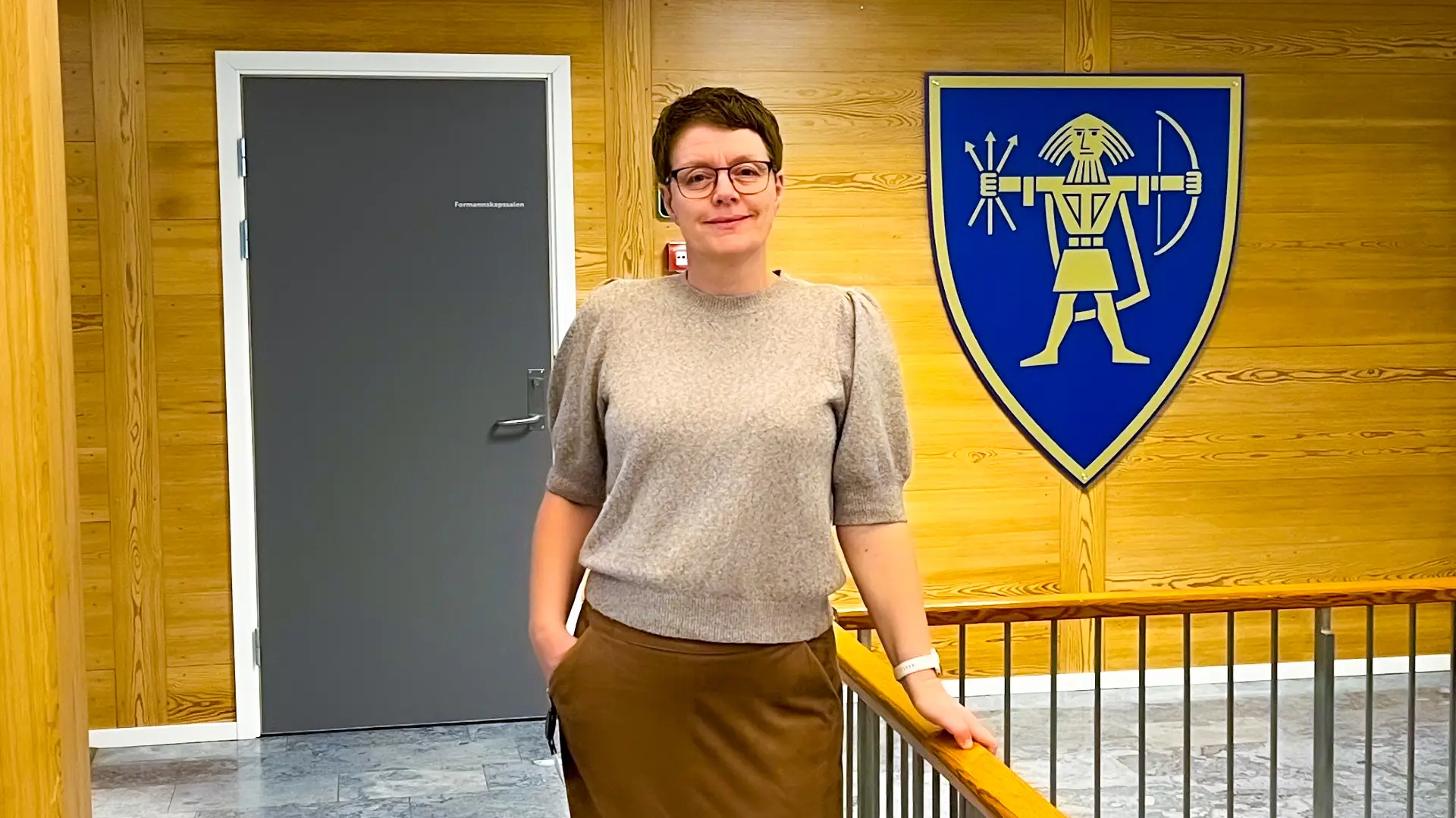 Bilde av Monica Ruud i gangen på rådhuset med kommunelogo i bakgrunnen