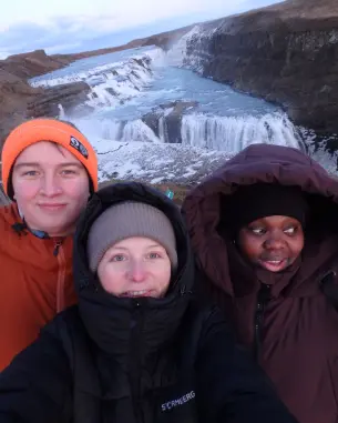 tre vinterkledde unge folk foran en mektig foss