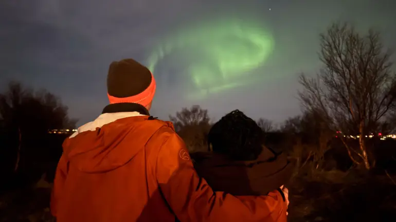 to unge personer står med ryggen til og ser på nordlys på himmelen