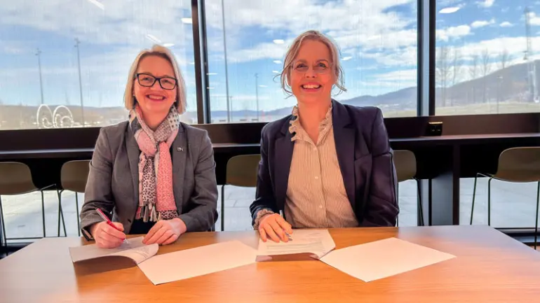 Bilde av Pia Bing Jonsson og Gøril Bergh som signerer avtale ved et bord