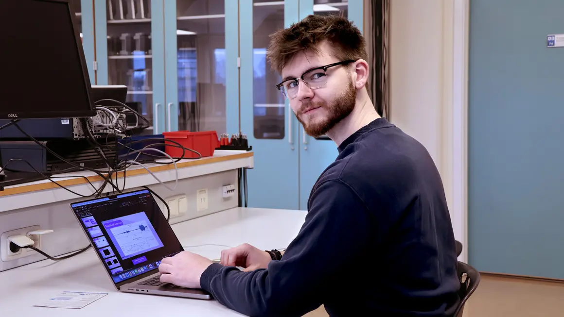 Christoffer i halvfigur sittende foran laptop og snur seg til kameram 