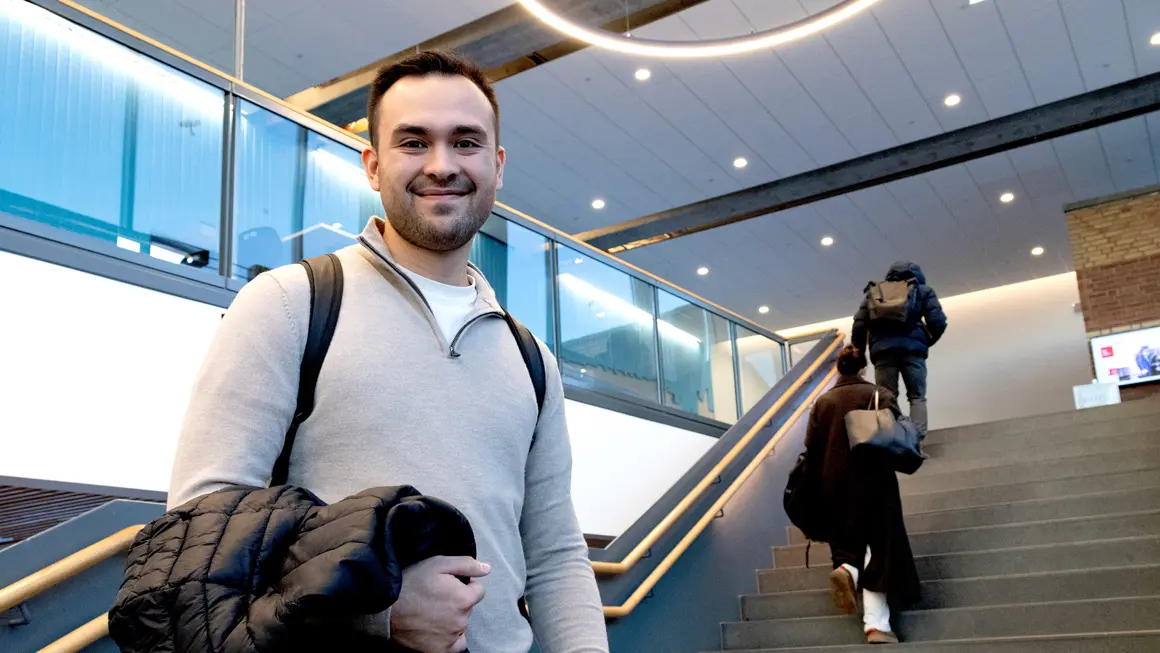 Alexander stående i hovedtrappa og ser i kamera på campus Vestfold 