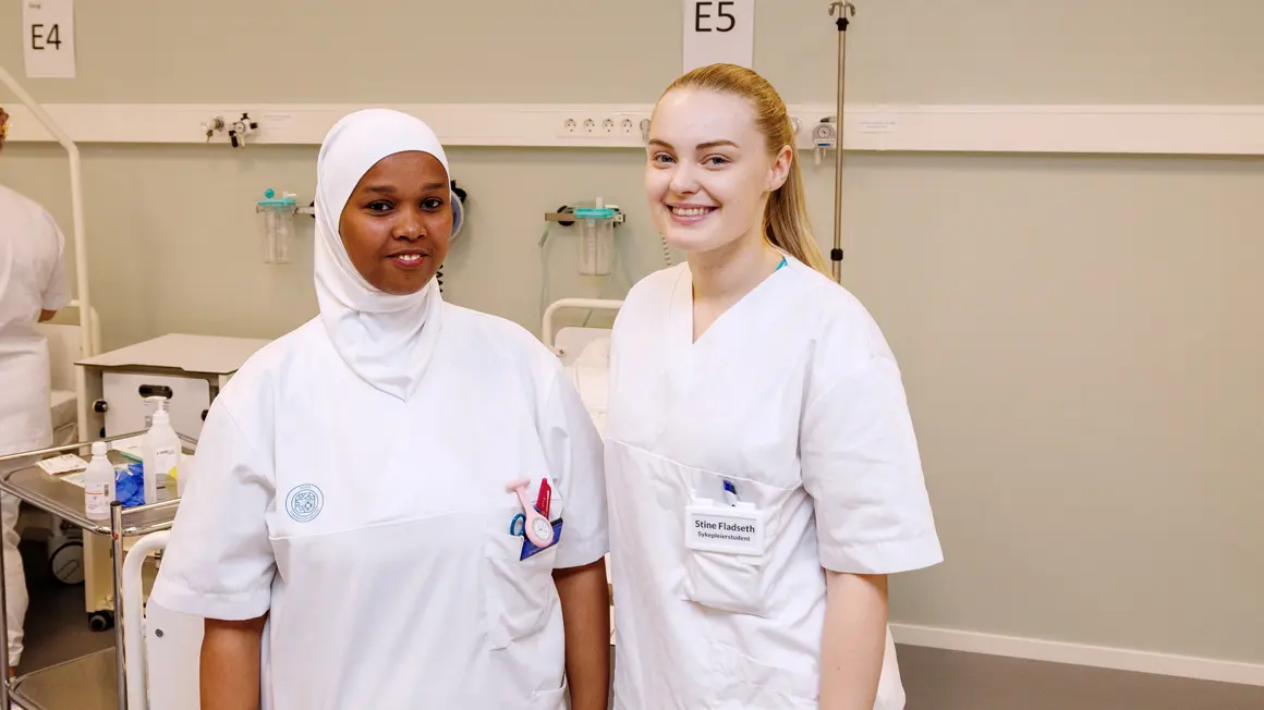 Najat Silh og Stine Fladseth i halvfigur på rekke smilende til kamera i hvite sykepleierklær