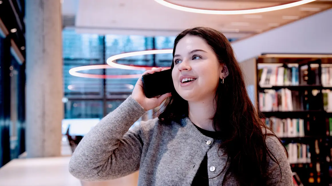 Simona md telefon til øret sittende på biblioteket på campus Vestfold og ser ut av vindu
