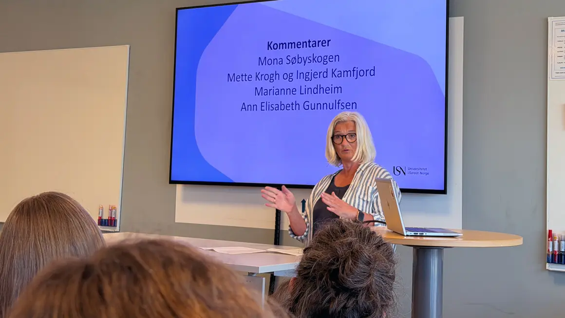 dame i stripete skjorte og hvitt hår presenterer foran skjerm