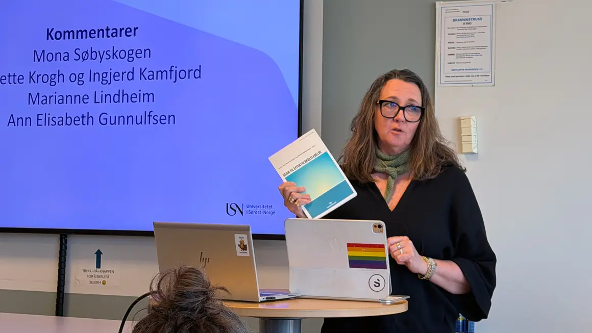 dame med briller står bak talerstol og holder forskningsrapport i hånda