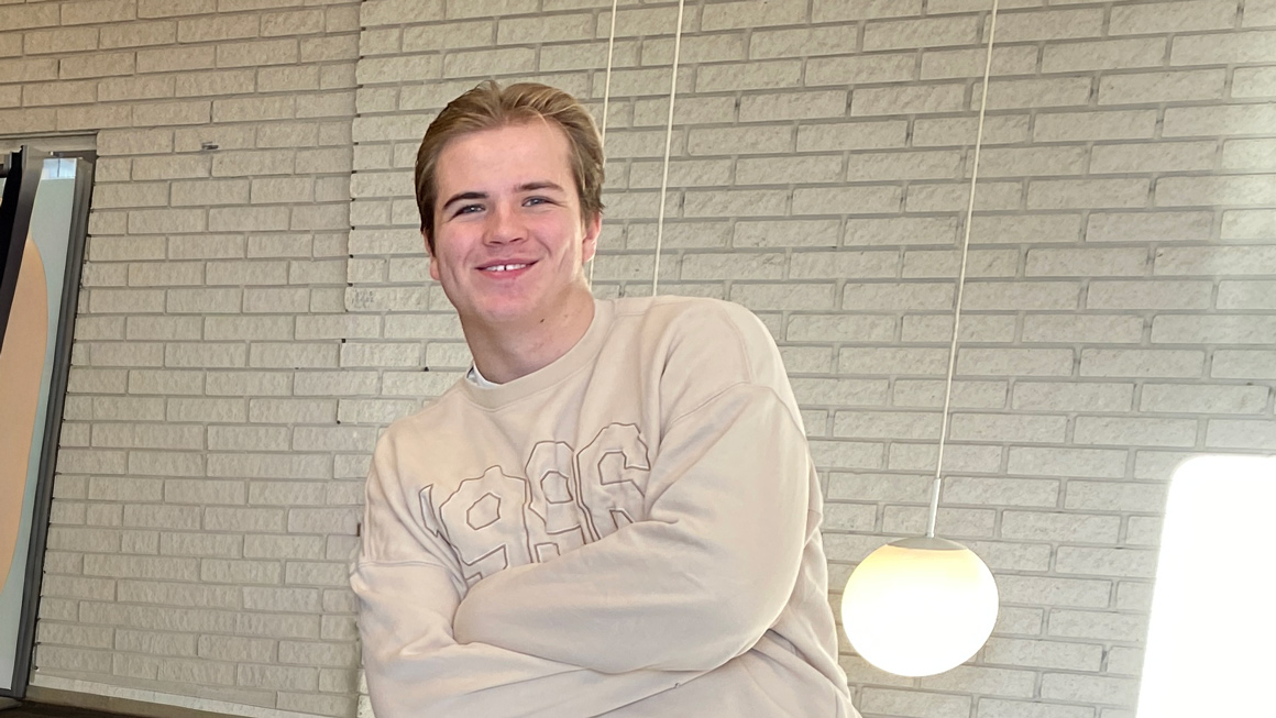 ung mann lener seg mot rekkverk og smiler i kameraet med armene i kryss