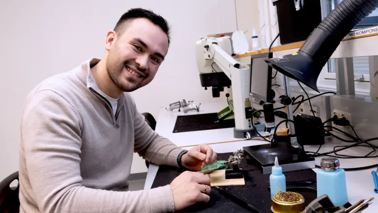 Alexander i elektronikklaben og jobber med sensorer og annet foran seg og snur seg mot kamera. d sensorer