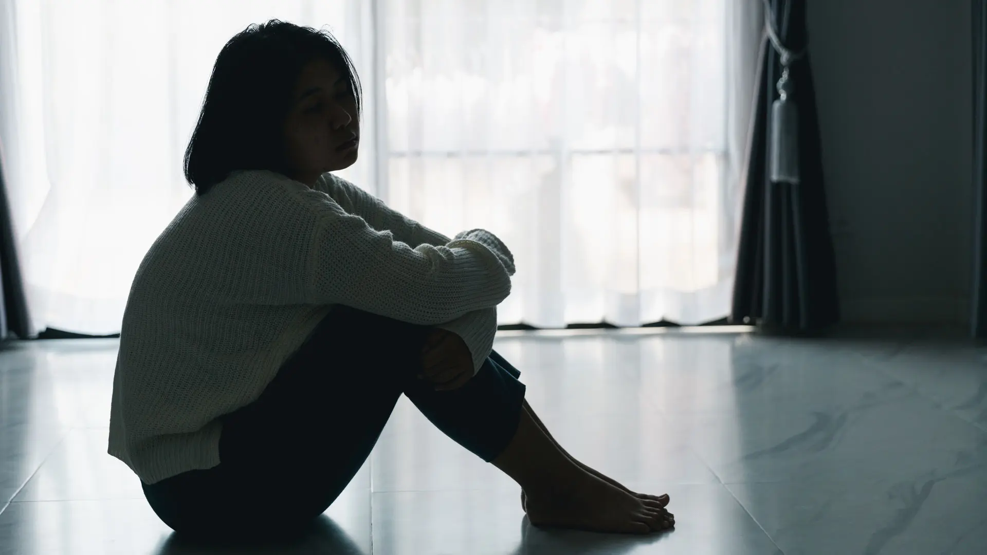 Ung jente sitter alene på gulvet i et halvmørkt rom
