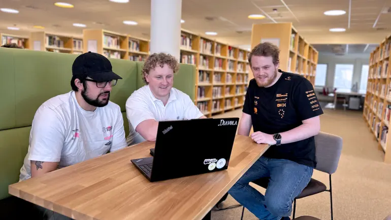 Jarand Byrkjeland i midten sittende rundt et bord med laptop foran seg omkranset av medstudentene Alan Alialy og Robin Danielsen.