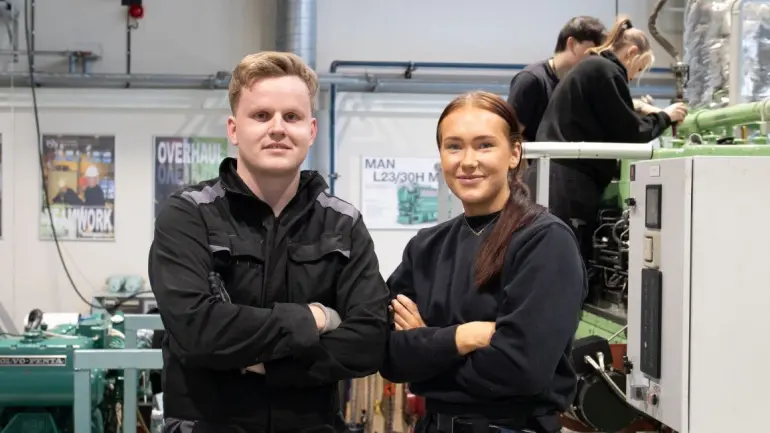 To ingeniørstudenter som står oppstilt og to som jobber i bakgrunn. Steffen Grimset Hagen og Silje Andersen på bachelor i maskinteknisk drift