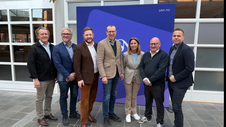 folk stilt opp på rekke foran USN-logo