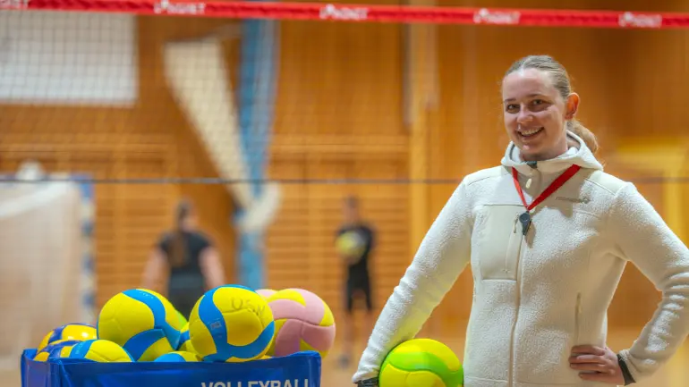 dame med volleyball under armen med nett i bakgrunnen