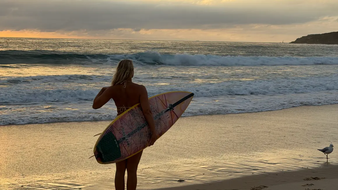 Student på stranden med surfebrett