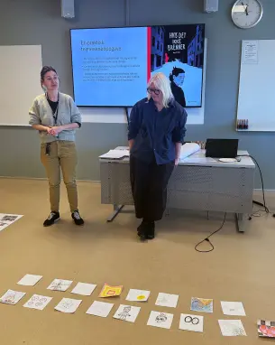 UNDERVISER: Adriana Margareta Dancus og Ingunn Vatnøy. to damer med tegneserier foran seg på gulvet i undervisningsrom