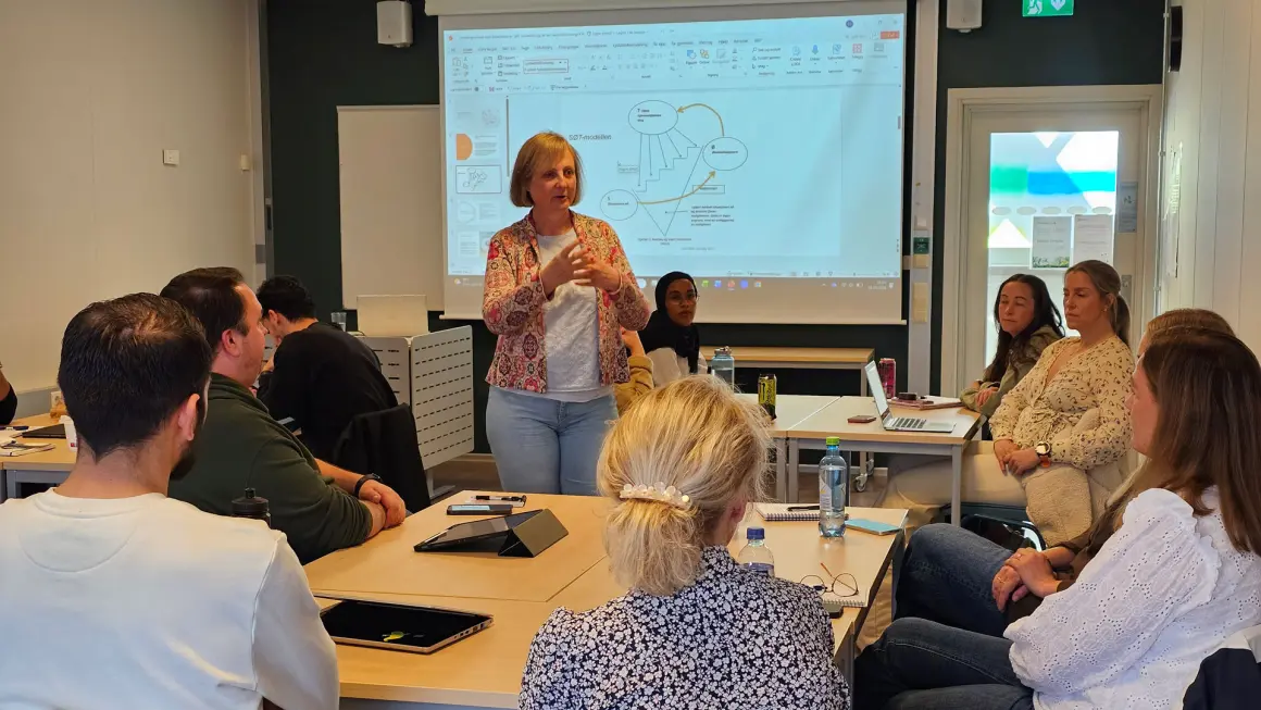 Eva Daae Kversøy underviser på videreutdanningen Teamledelse på sengepost i spesialisthelsetjenesten.. Fotograf: Maren Sofie Sandbakk Bilde av foreleser Eva Daae Kversøy inne i klasserommet i samtale med studenter.