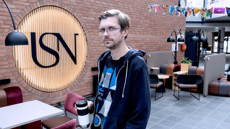 UNIVERSITET I NÆRHETEN: – Å ha et universitet der vi bor, har gjort det mye enklere å ta høyere utdanning, sier Petter Tangvald Fevang, som bor i Skien og studerer i nabobyen på USN campus Porsgrunn. (Foto: An-Magritt Larsen) Petter gående med termokoppen i hånda og ser i kamera. har briller. Glassgata på campus Porsgrunn ikledd mørk t-skjorte og hettejakke.