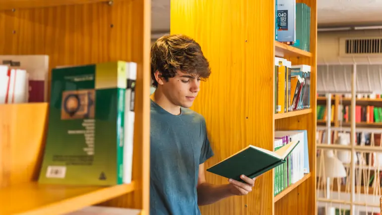 Ung gutt leser en bok mellom bokhyller