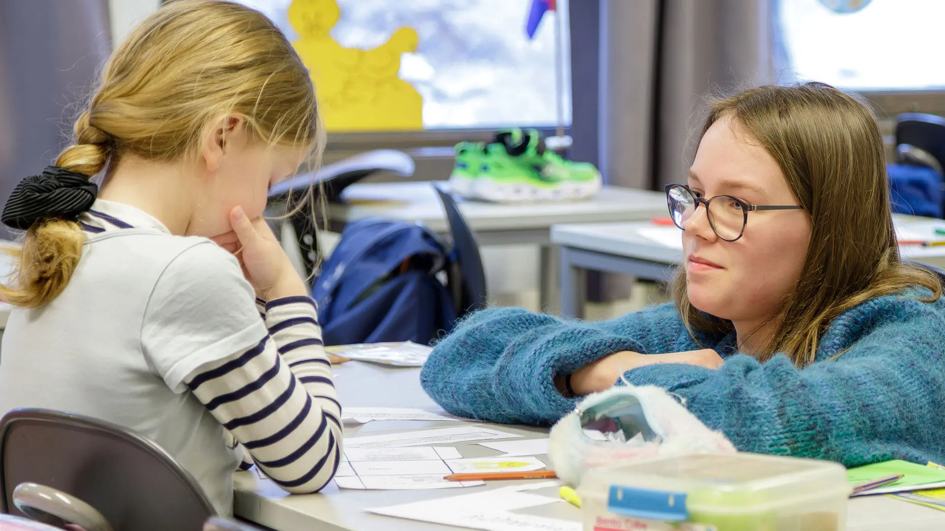 lærer bøyer seg ned og snakker med en førsteklassing ved pulten