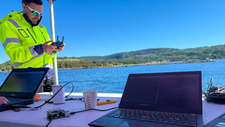 Fotograf: Jan-Henrik Kulberg Professor Fabio Augusto de Alcantara Andrade står med en dronekontroll i hendene ved siden av en bærbar datamaskin, med blått vann og fjell i bakgrunnen.