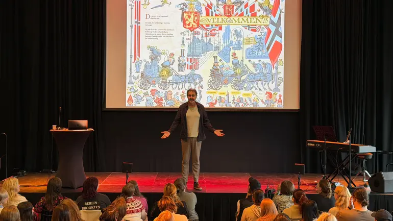 illustratør Svein Nyhus på scenen med fargerik illustrasjon i bakgrunnen som sier "velkommen"