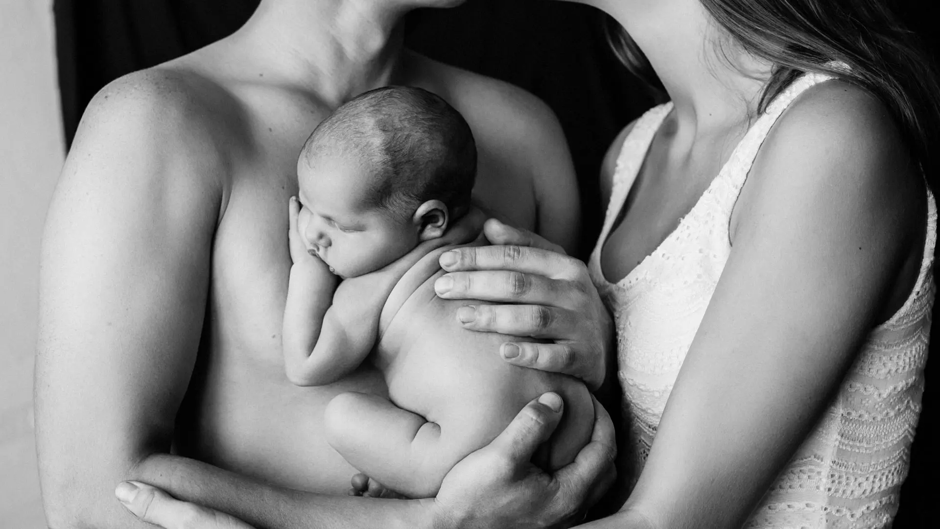 Svarthvitt nærbilde av voksne som holder en nyfødt baby i armene sine