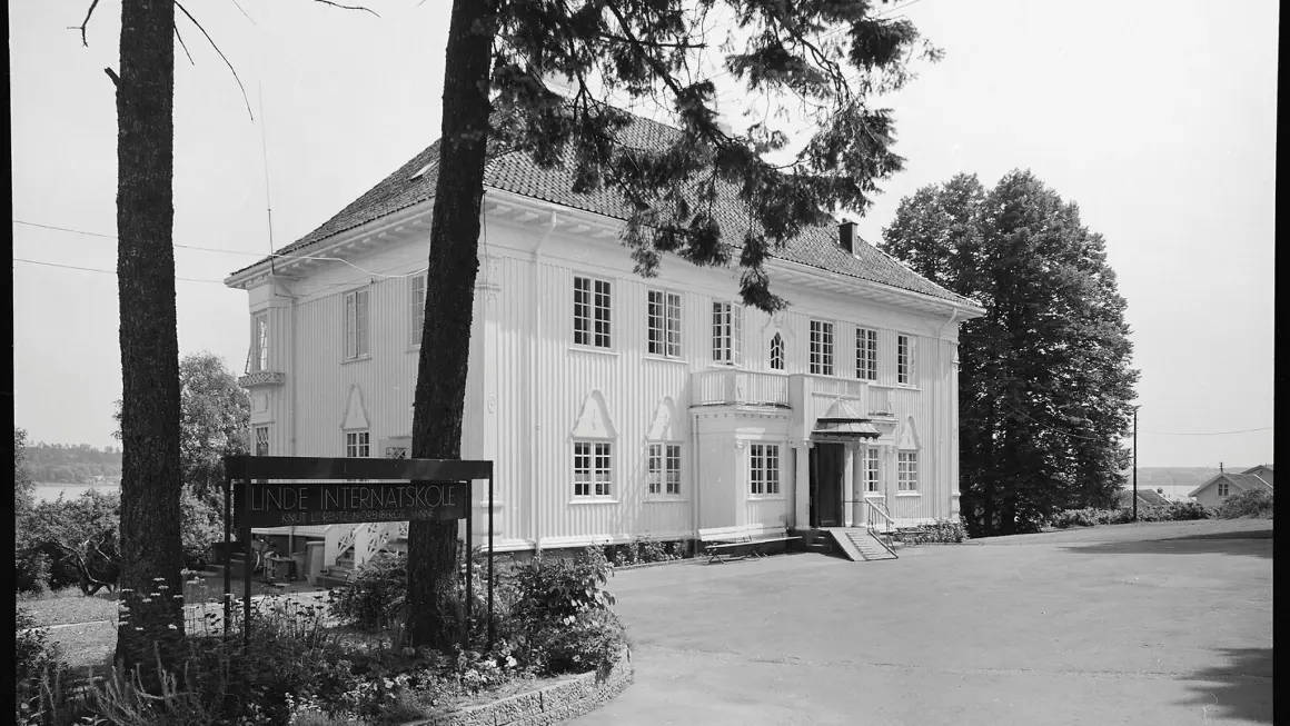 Linde internatskole fotografert i 1969. Gjengitt med tillatelse fra Vestfoldmuseene. Foto: Fotograf Wittek, Slottsfjellmuseets fotosamling Svarthvitt bilde av et hus med et skilt og noen trær foran