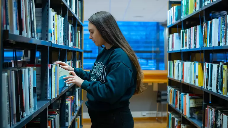 Viktoria Wikstrøm ser gjennom hyllene på biblioteket på campus Vestfold.