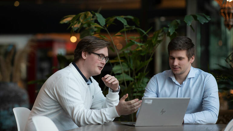 Håkon sittende sammen med sjefen Kristoffer Karud, ser i en laptop på bordet. Blurry bakgrunn i kontorlandskap.