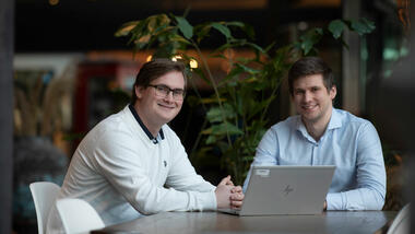 Håkon sittende sammen med sjefen sin, Kristoffer Karud, i Telenors lokaler med laptop foran dem på bordet. 
